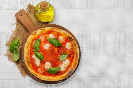 Foto de Pizza de margarita casera, cubierta con tomates frescos, queso mozzarella y hojas aromáticas de albahaca. En la mesa de jardín al aire libre plana con espacio de copia - Imagen libre de derechos