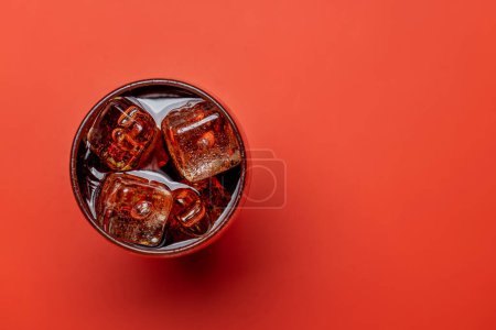 Téléchargez les photos : Verre rafraîchissant de cola avec glace. Sur fond rouge avec espace de copie. Pose plate - en image libre de droit