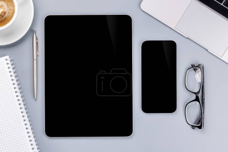 Photo for Tablet and smartphone with blank screen on business office desk. Flat lay workspace with sunny light and copy space - Royalty Free Image