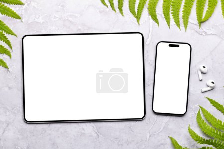 Photo for Smartphone and tablet with blank screen on a table surrounded by green nature leaves, perfect design mockup - Royalty Free Image
