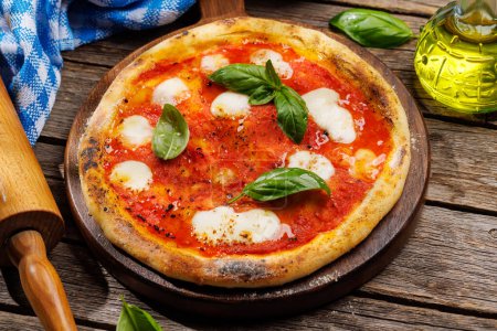 Foto de Pizza de margarita casera, cubierta con tomates frescos, queso mozzarella y hojas aromáticas de albahaca. En la mesa de jardín al aire libre - Imagen libre de derechos