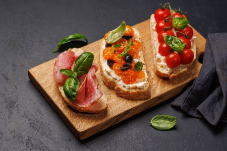 Foto de Un delicioso sándwich de bruschetta adornado con jugosos tomates, queso y salado prosciutto - Imagen libre de derechos