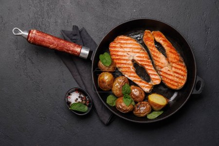 Téléchargez les photos : Des steaks de saumon grillés et des pommes de terre dans une poêle, un délice appétissant. Pose plate avec espace de copie - en image libre de droit