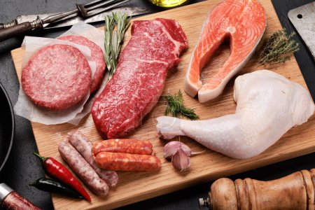 Foto de Varias carnes crudas y pescado. Filetes, salchichas, salmón, pollo y especias en la tabla de cortar - Imagen libre de derechos