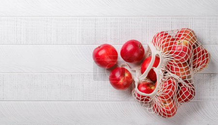 Photo for Mesh bag with fresh red apples on wood table. Flat lay with copy space - Royalty Free Image