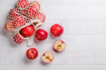 Téléchargez les photos : Sac en maille avec pommes rouges fraîches sur table en bois. Pose plate avec espace de copie - en image libre de droit