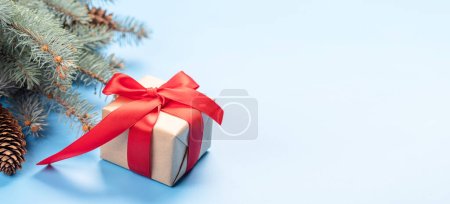 Photo for Christmas fir tree branch and gift box over blue background with space for greetings text - Royalty Free Image