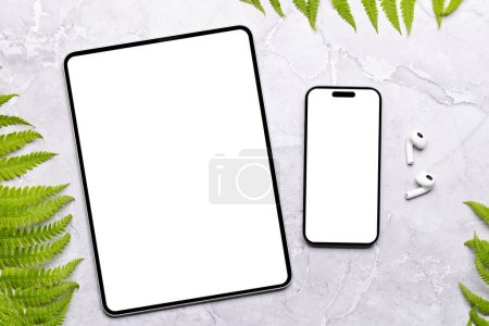 Foto de Smartphone y tableta con pantalla en blanco en una mesa rodeada de hojas verdes de la naturaleza, maqueta de diseño perfecto - Imagen libre de derechos