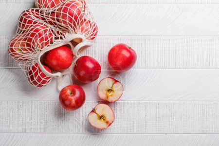 Photo for Mesh bag with fresh red apples on wood table. Flat lay with copy space - Royalty Free Image