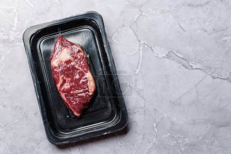 Téléchargez les photos : Bifteck de côtelette de bœuf cru frais scellé dans un emballage sous vide, préservant sa qualité et sa fraîcheur. Pose plate avec espace de copie - en image libre de droit