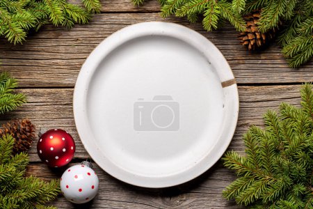 Téléchargez les photos : Cadre de table d'en haut avec assiette vide, branches de sapin de Noël et cônes de pin sur fond en bois. Pose plate - en image libre de droit