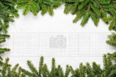 Photo for Christmas fir tree branch frame over white wood with space for greetings text. Flat lay - Royalty Free Image