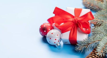 Téléchargez les photos : Branche de sapin de Noël, boîte cadeau et décor boule sur fond bleu avec espace pour salutations texte - en image libre de droit