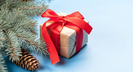 Téléchargez les photos : Branche sapin de Noël et boîte cadeau sur fond bleu avec espace pour salutations texte - en image libre de droit