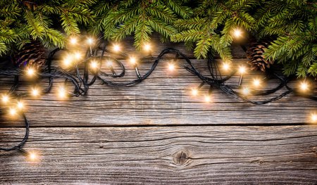 Photo for Christmas glowing garland and fir tree branches on wooden background with copy space - Royalty Free Image