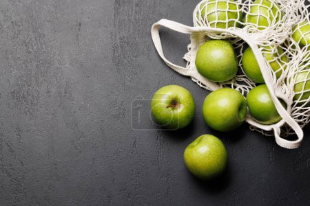 Téléchargez les photos : Sac en maille avec pommes vertes fraîches sur table en pierre. Pose plate avec espace de copie - en image libre de droit