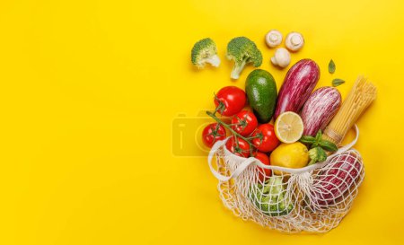 Foto de Bolsa de malla llena de una variedad de verduras. Piso sobre fondo amarillo con espacio de copia - Imagen libre de derechos