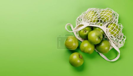 Photo for Mesh bag with fresh green apples over green background. Flat lay with copy space - Royalty Free Image