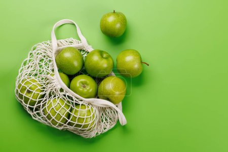 Photo for Mesh bag with fresh green apples over green background. Flat lay with copy space - Royalty Free Image