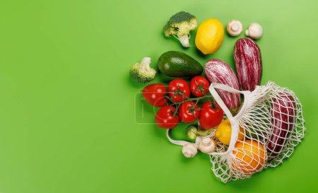 Photo for Mesh bag filled with a variety of vegetables. Flat lay over green background with copy space - Royalty Free Image