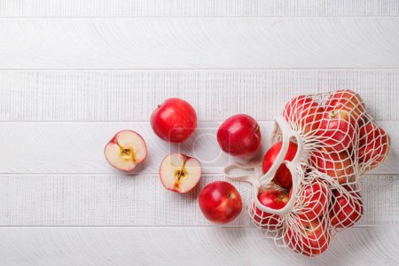 Téléchargez les photos : Sac en maille avec pommes rouges fraîches sur table en bois. Pose plate avec espace de copie - en image libre de droit