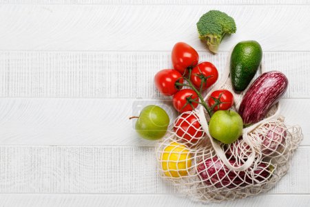 Photo for Mesh bag filled with a variety of vegetables. Flat lay over white wooden background with copy space - Royalty Free Image