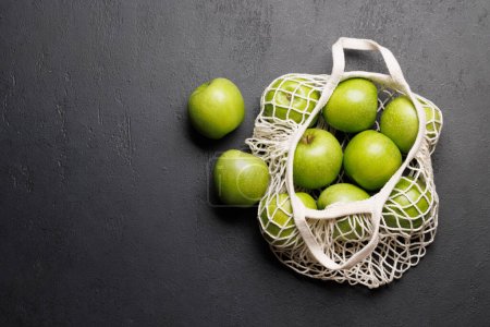 Photo for Mesh bag with fresh green apples on stone table. Flat lay with copy space - Royalty Free Image