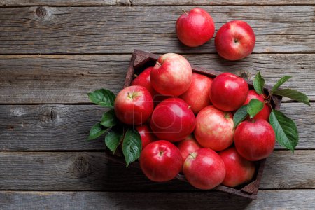 Téléchargez les photos : Boîte en bois avec pommes rouges fraîches sur table en bois. Pose plate avec espace de copie - en image libre de droit