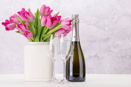 Photo for Fresh pink tulip flowers bouquet and champagne. On white wooden table with copy space - Royalty Free Image
