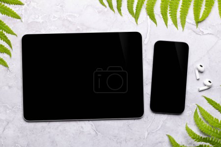 Foto de Smartphone y tableta con pantalla en blanco en una mesa rodeada de hojas verdes de la naturaleza, maqueta de diseño perfecto - Imagen libre de derechos