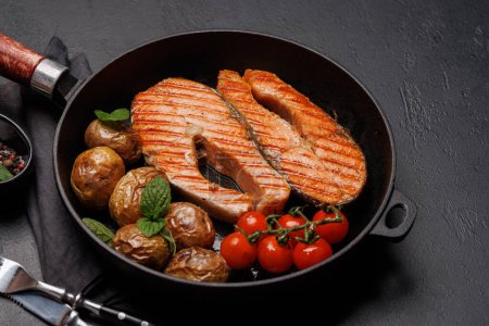 Photo for Grilled salmon steaks and potatoes sizzling in a frying pan, a mouthwatering delight - Royalty Free Image