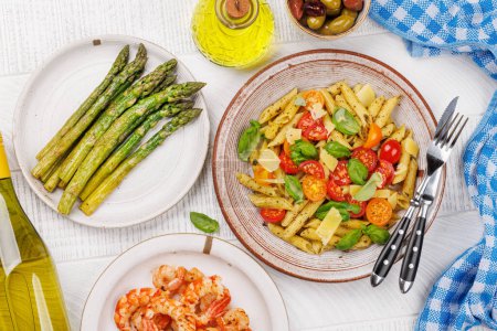 Téléchargez les photos : Assiette délicieuse de pâtes italiennes ornée de tomates fraîches et de feuilles de basilic aromatiques, d'asperges grillées et de crevettes. Pose plate - en image libre de droit