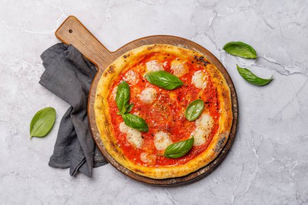 Foto de Pizza de margarita casera, cubierta con tomates frescos, queso mozzarella y hojas aromáticas de albahaca. Puesta plana - Imagen libre de derechos