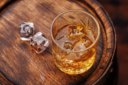 Foto de Vaso de whisky con hielo en un barril rústico, un sorbo clásico. Primer plano. - Imagen libre de derechos
