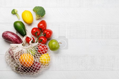 Photo for Mesh bag filled with a variety of vegetables. Flat lay over white wooden background with copy space - Royalty Free Image