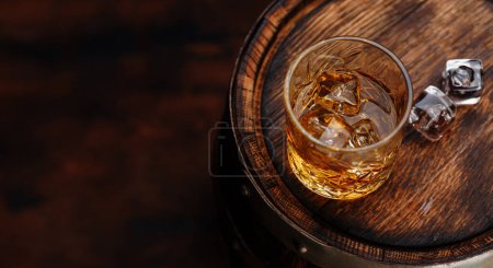Whiskey glass with ice on a rustic barrel, a classic sip. With copy space
