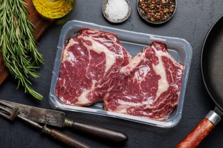 Photo for Raw ribeye steaks in package and savory spices. Flat lay - Royalty Free Image