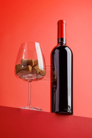 Téléchargez les photos : Élégance du vin rouge : Verre à vin avec bouchons et bouteille sur fond rouge vif. Avec espace de copie - en image libre de droit