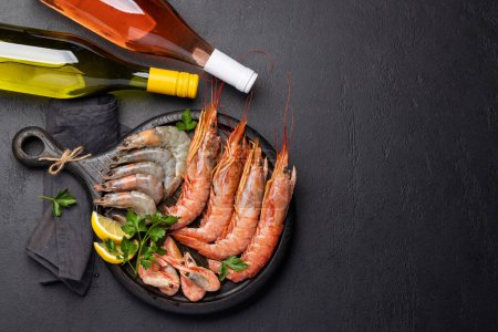 Téléchargez les photos : Une vue imprenable sur les fruits de mer frais tels que les crevettes, les langoustines et les steaks de truite, accompagnés de vin blanc et rose. Pose plate avec espace de copie - en image libre de droit