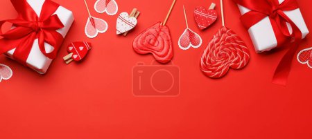 Téléchargez les photos : Sucettes de coeur : friandises sucrées et boîtes-cadeaux sur fond rouge avec espace texte. Pose plate carte Saint Valentin - en image libre de droit