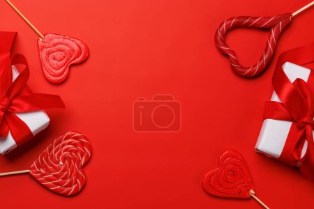 Foto de Piruletas del corazón: Dulces y cajas de regalo sobre un fondo rojo con espacio de texto. Flat lay tarjeta de San Valentín - Imagen libre de derechos