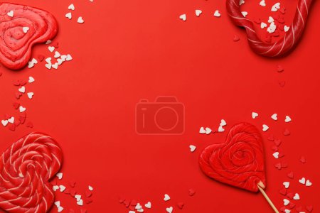 Foto de Piruletas del corazón: Dulces golosinas sobre un telón de fondo rojo con espacio de texto. Flat lay tarjeta de San Valentín - Imagen libre de derechos