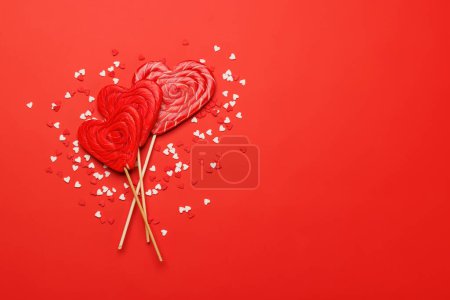 Téléchargez les photos : Sucettes de coeur : sucreries sucrées sur fond rouge avec espace de texte. Pose plate carte Saint Valentin - en image libre de droit