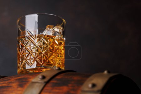 Téléchargez les photos : Verre à whisky avec glace sur un tonneau rustique, une gorgée classique. Avec espace de copie - en image libre de droit
