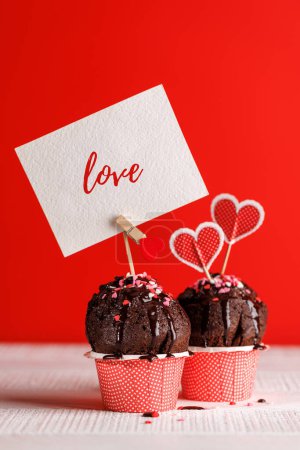 Photo for Cupcake love: Heart-themed treats on a vibrant red backdrop with copy space for your Valentines day greetings - Royalty Free Image