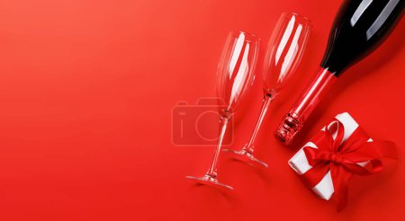 Foto de Champán y regalo: Dúo de celebración sobre fondo rojo con espacio de texto. Tarjeta de felicitación de San Valentín - Imagen libre de derechos