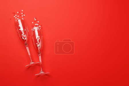 Téléchargez les photos : Verres à champagne avec bonbons au cœur sur fond rouge avec espace texte. Carte de voeux Saint-Valentin - en image libre de droit