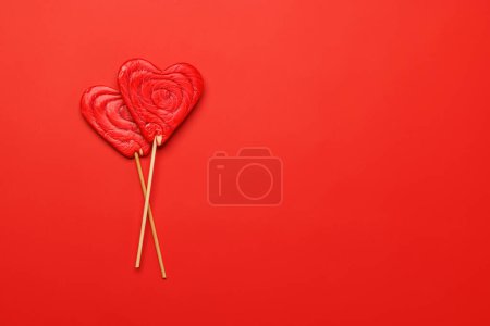 Foto de Piruletas del corazón: Dulces golosinas sobre un telón de fondo rojo con espacio de texto. Flat lay tarjeta de San Valentín - Imagen libre de derechos