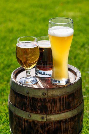 Téléchargez les photos : Variété de verres à bière sur tonneau en bois rustique. Ensoleillé extérieur avec espace de copie - en image libre de droit
