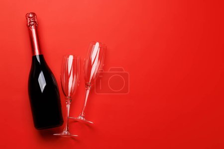 Téléchargez les photos : Verres à champagne et bouteille sur fond rouge avec espace texte. Carte de voeux Saint-Valentin - en image libre de droit